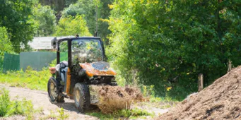Un micro tracteur transportant du sable dans un champ agricole avec un chargeur frontal.