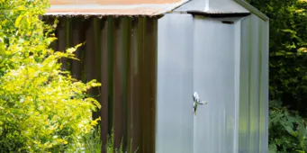 Un petit abri de jardin en métal robuste avec un fond de verdure